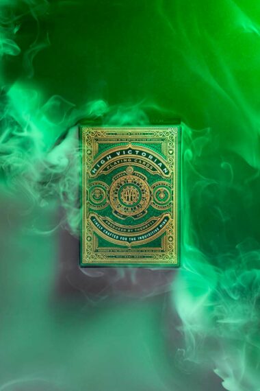 Photographie vue de face d'un jeu de cartes vert avec des dorures "high victorian" de chez Theory 11 sur fond vert avec une diagonale de fumée